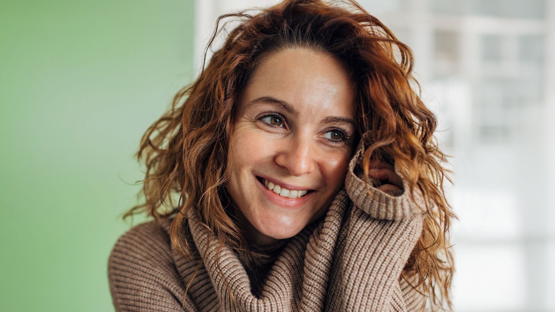 Lächelnde Frau mit lockigem Haar, die einen gemütlichen Pullover trägt.
